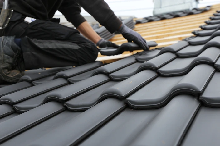 Ouvrier couvreur en tenue de travail noire installant des tuiles sur une toiture en cours de construction
