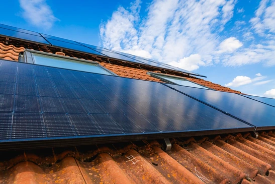 Ouvrier installant des panneaux solaires sur une toiture en plein air, utilisant un outil de levage à ventouses rouges pour manipuler les modules photovoltaïques