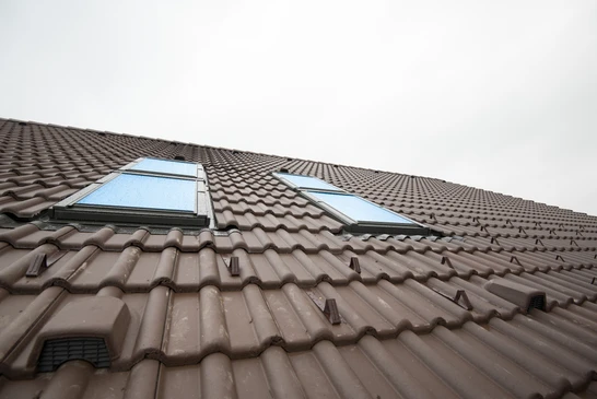 Artisan en vêtements de travail installe une fenêtre de toit dans les combles d'une habitation