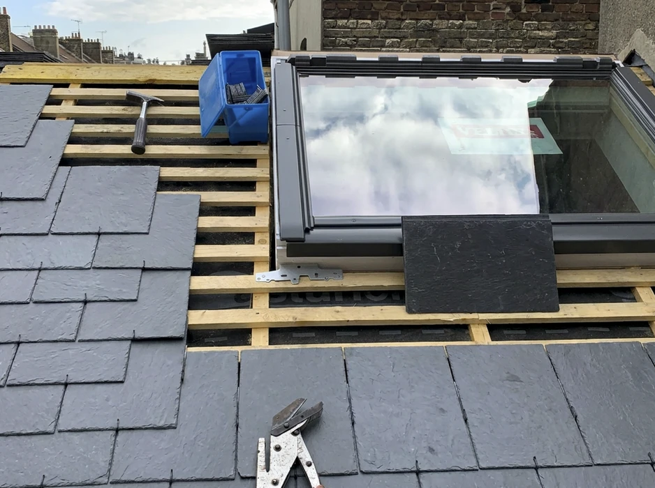 Ouvrier couvreur en tenue de travail noire installant des tuiles sur une toiture en cours de construction