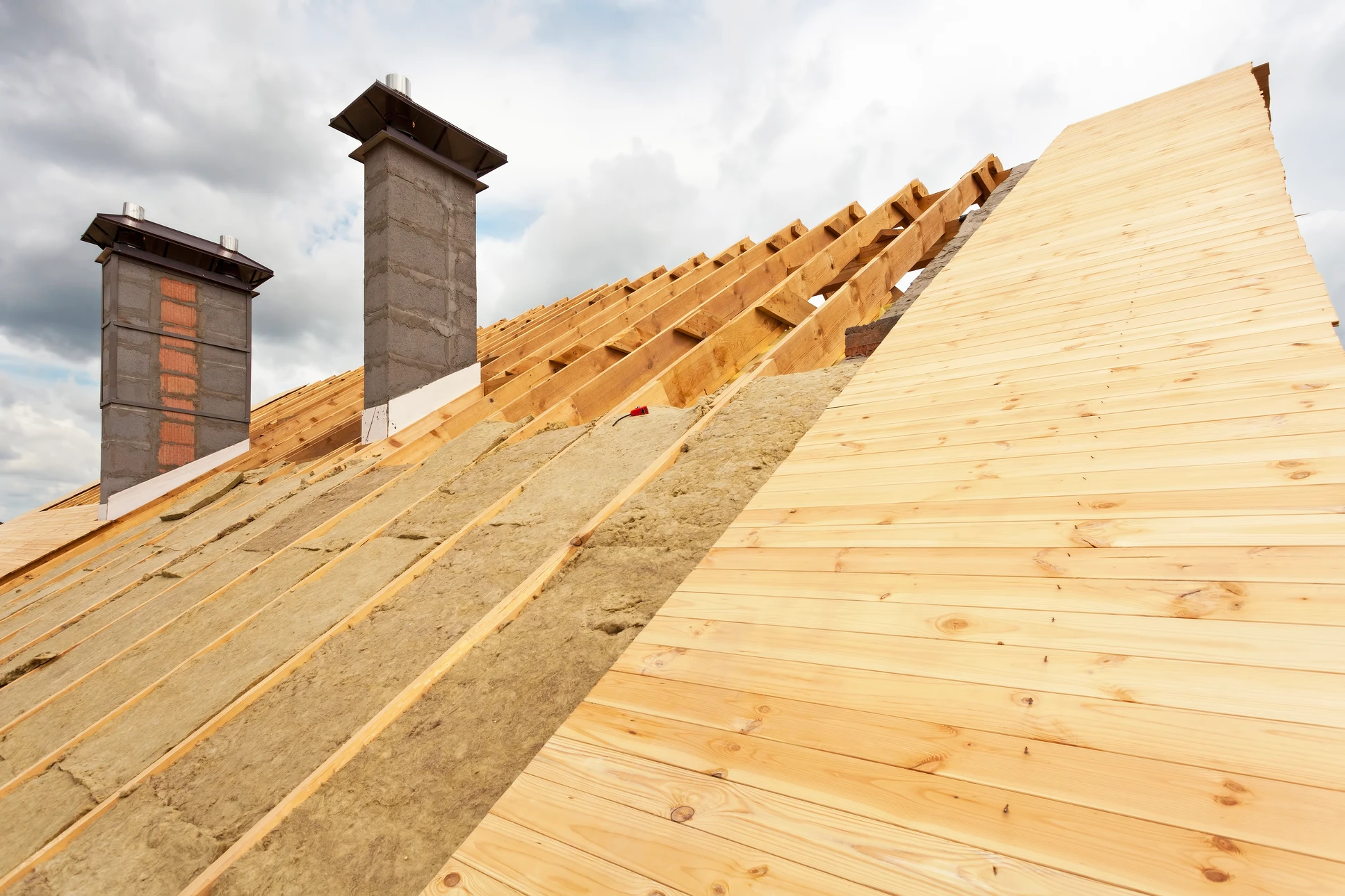 Chantier de rénovation de combles avec charpente bois apparente, isolation en laine minérale verte entre chevrons