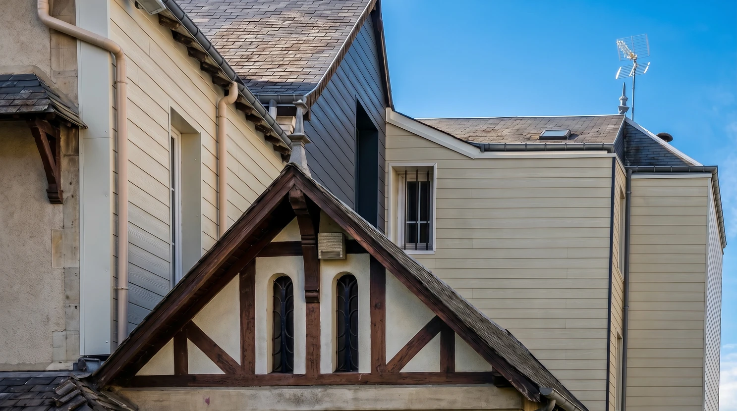 Toiture résidentielle moderne avec couverture en ardoises grises, lucarnes à volets noirs, cheminée maçonnée et fenêtres de toit